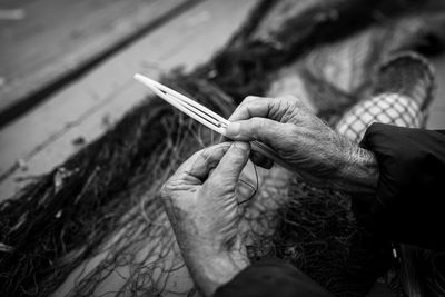 Cropped hand of woman holding thread while sitting outdoors