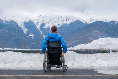 Rear view of man sitting on snow covered mountain