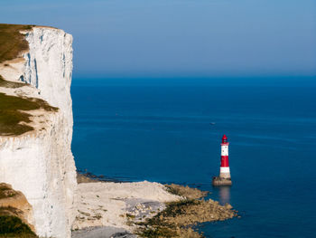 Lighthouse by sea against blue sky