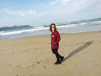 Full length portrait of smiling woman standing at beach