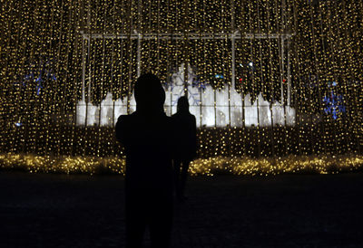 Rear view of silhouette man standing against illuminated light at night