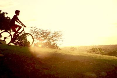 Silhouette man riding bicycle on field against sky during sunset