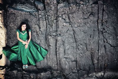Portrait of smiling woman wearing green dress while standing on rock formation