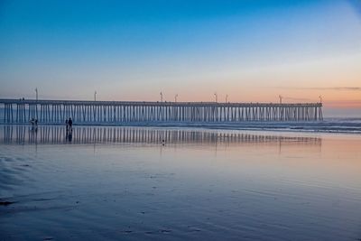 Pier on beach against clear sky during sunset