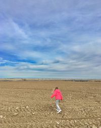 Young girl walking on field against sky