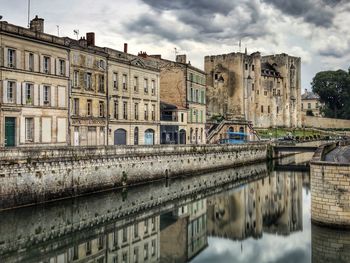 Bridge over river by buildings against sky