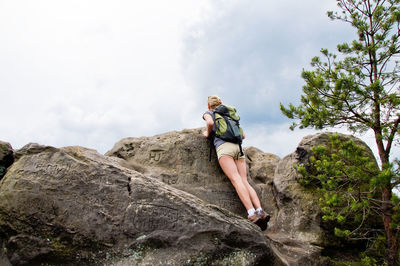 Low angle view of young woman leaning on rock against sky