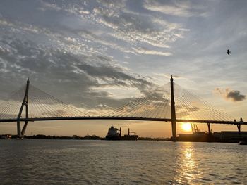 View of suspension bridge over river against cloudy sky