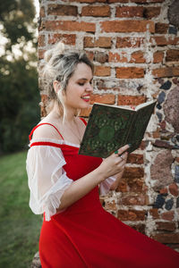 Woman holding red while standing against wall