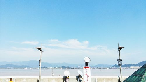 People on walkway by river during sunny day