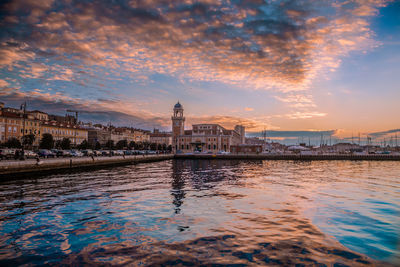 Bridge over river by buildings against sky during sunset