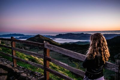 Rear view of woman looking at mountains against sky during sunset