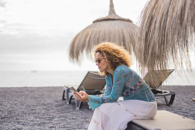 Young woman using mobile phone while sitting on shore