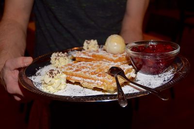 Midsection of man holding waffle with ice cream and cranberry sauce in plate