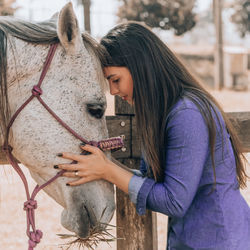 Side view of woman touching horse in barn