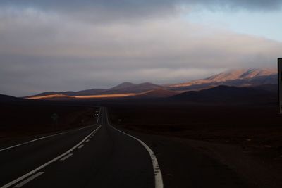 Empty road leading towards mountains against sky