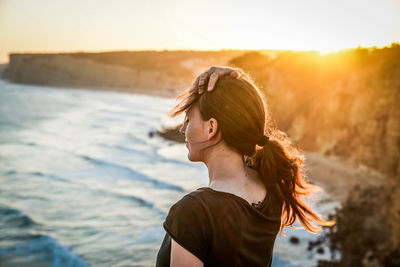 Young woman with hand in hair standing against seashore