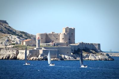 Sailboats in sea by buildings against clear blue sky