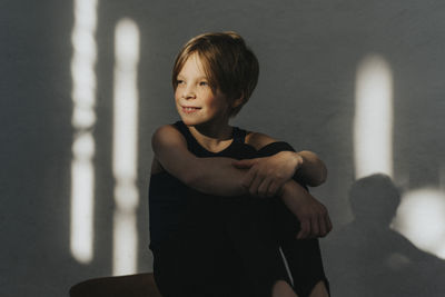 Contemplative elementary boy looking away while sitting against wall