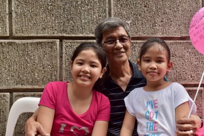 Portrait of smiling girls sitting with grandfather against wall