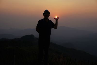 Optical illusion of silhouette man holding sun against sky during sunset