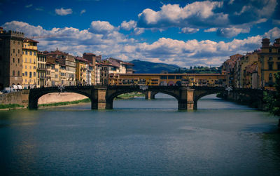 Medieval ponte vecchio bridge over the arno river under a blue cloudy sky in florence