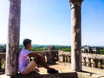 Side view of young man sitting against sky