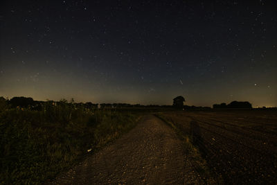 Dirt road amidst field against sky at night