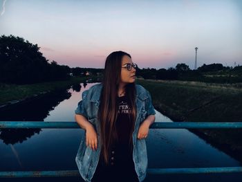 Beautiful young woman standing by sea against sky during sunset