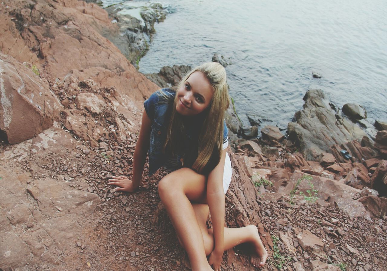 water, lifestyles, person, leisure activity, young adult, high angle view, casual clothing, portrait, looking at camera, full length, sitting, standing, young women, day, front view, rock - object, outdoors, smiling