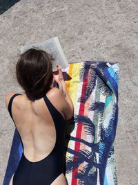 Rear view of woman reading book while lying on front at beach