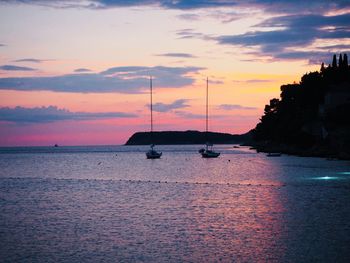 Silhouette sailboats in sea against sky during sunset