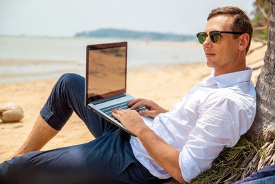 Portrait of woman using laptop while sitting at beach