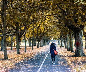 Rear view of woman walking on road along trees