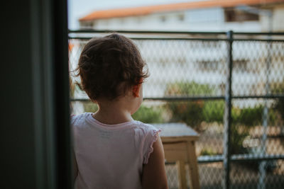 Rear view of baby girl looking through window while standing at home