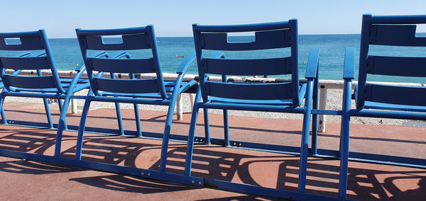 Empty chairs on beach against blue sky