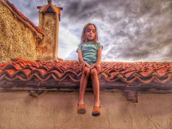 Full length portrait of girl sitting on stone wall