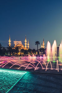 Illuminated fountain in city against clear sky at night