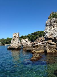 Rocks in sea against clear blue sky