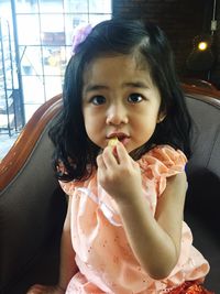 Close-up portrait of girl eating food on chair at home