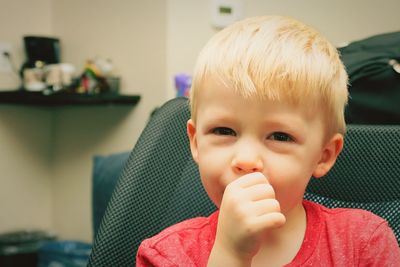 Portrait of cute boy with finger in mouth at home