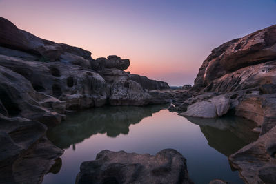 Rock formation in lake against sky during sunset