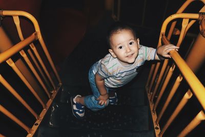 High angle portrait of cute boy standing on steps of slide at night