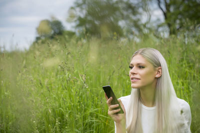 Portrait of young woman holding smart phone while standing on field