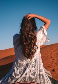 Rear view of woman riding on camel in desert against sky