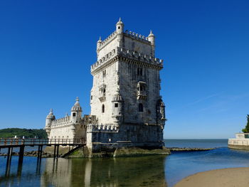 Tower by sea against clear blue sky