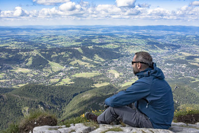 Hiker sitting on cliff by landscape against sky