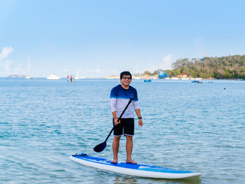 Asian man in casual clothes standing on paddleboard on blue sea water 