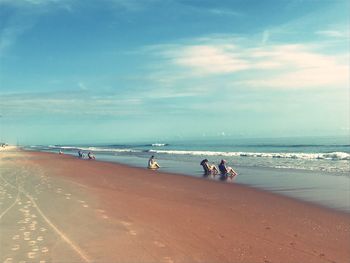 People resting on shore at beach against sky