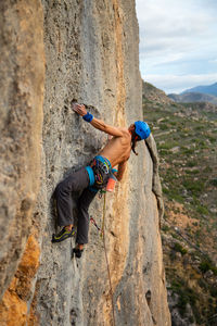 Shirtless man rock climbing against sky